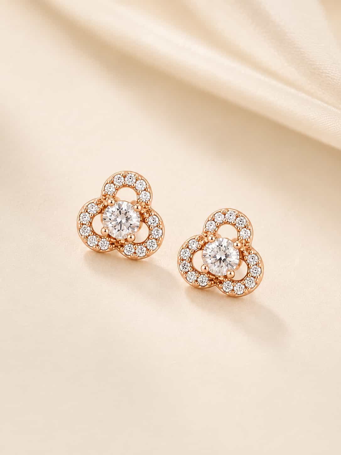 Rose gold floral halo stud earrings displayed together on soft cream satin fabric