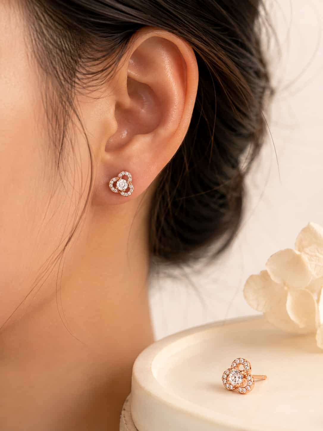 Rose gold floral halo stud earring worn on ear with matching stud displayed beside it