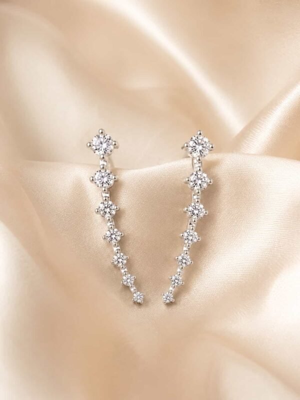 Close-up of silver-tone ear climber earrings with graduated clear round stones on cream satin