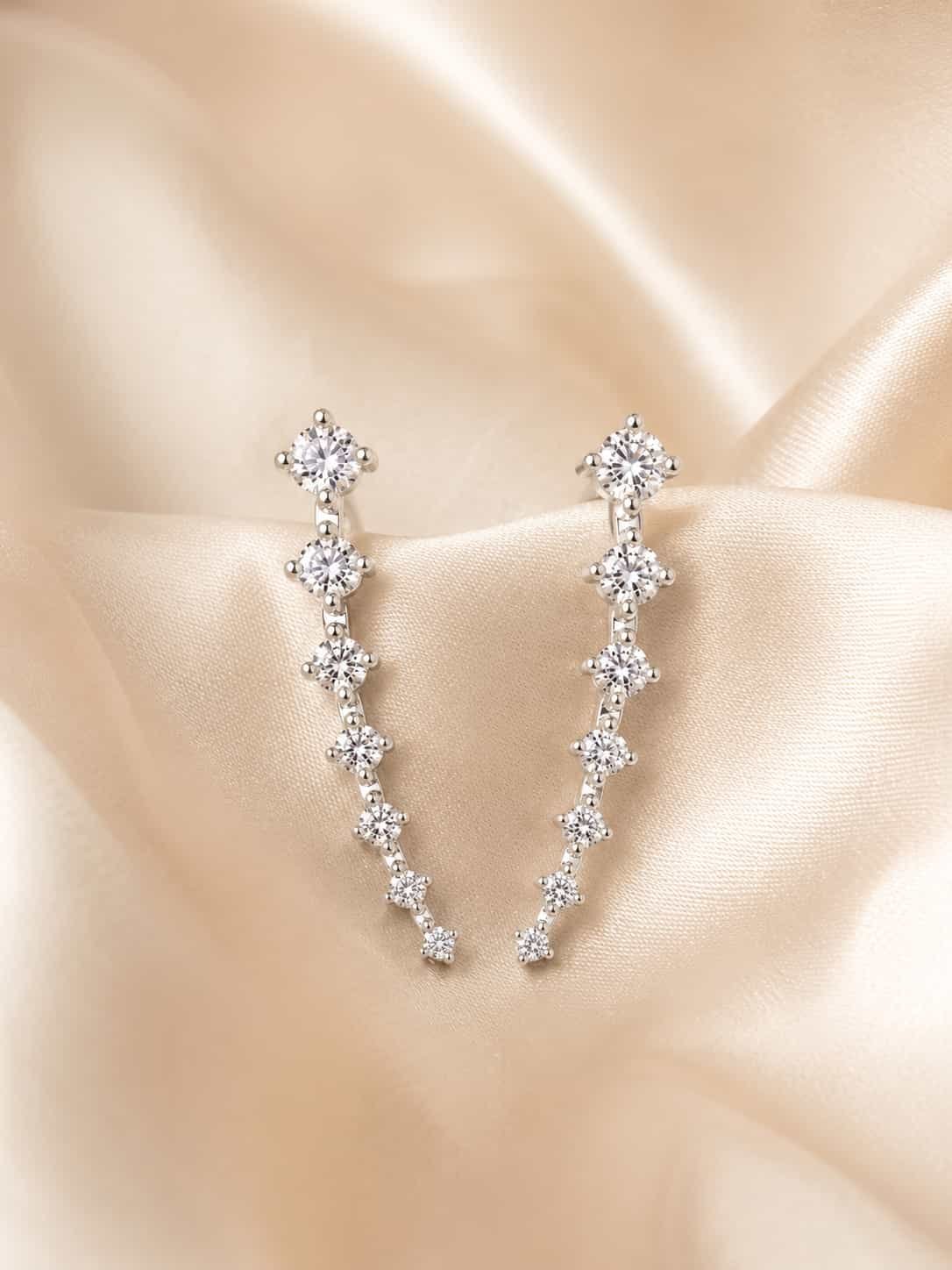Close-up of silver-tone ear climber earrings with graduated clear round stones on cream satin