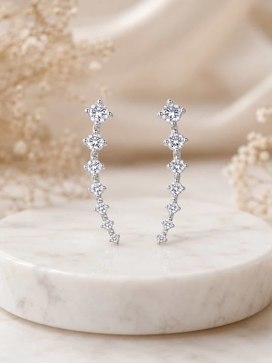 Pair of silver-tone graduated stone ear climber earrings shown upright on a white marble display