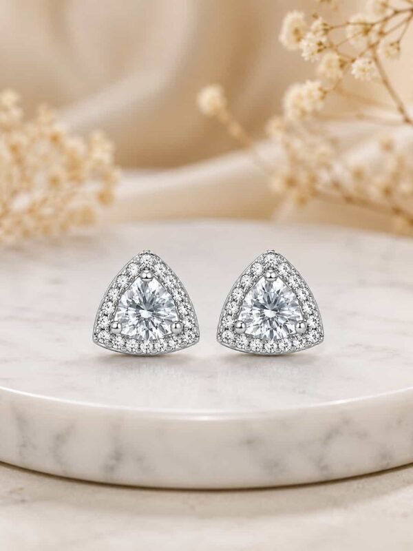 Platinum polished triangle halo stud earrings displayed on cream marble pedestal
