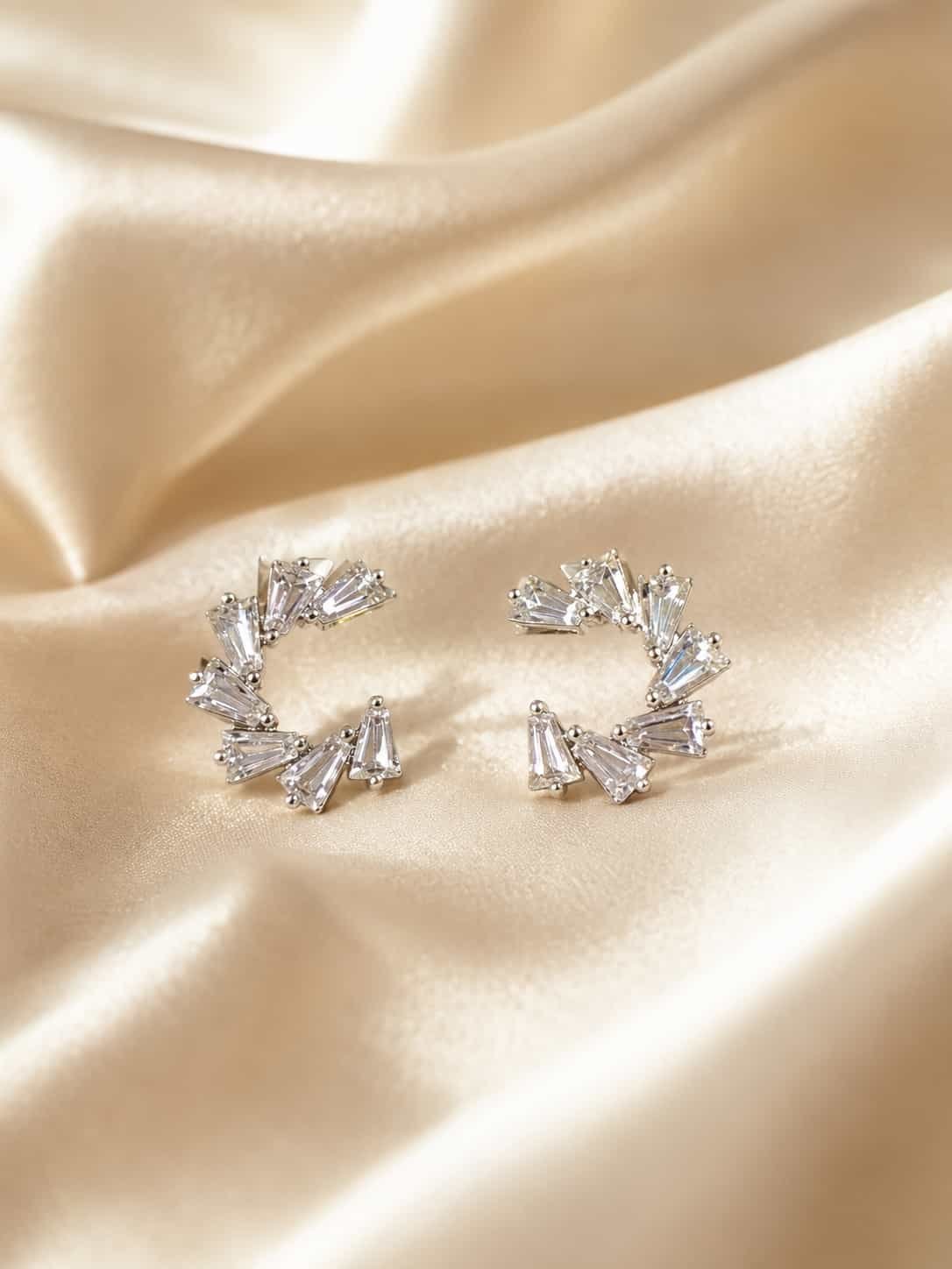Platinum polished crystal fan earrings with tapered stones displayed on soft champagne satin