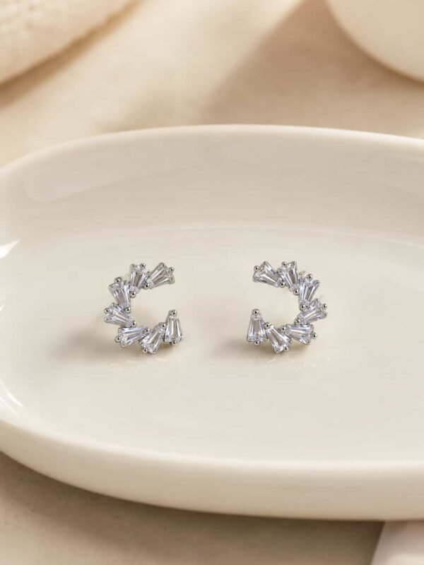 Platinum polished crystal fan open hoop earrings with tapered clear stones on a cream ceramic display