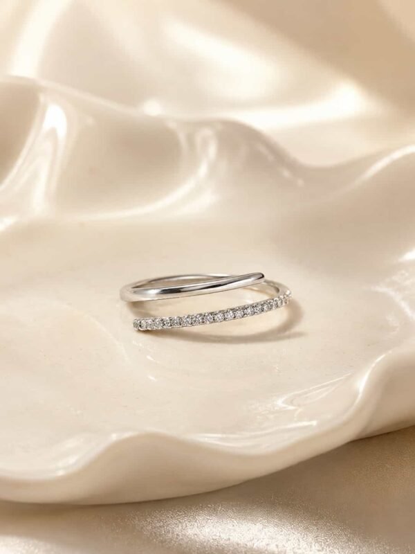 Close-up of the Naira double-row open wrap ring with a polished band and sparkling clear stones on a white ceramic tray