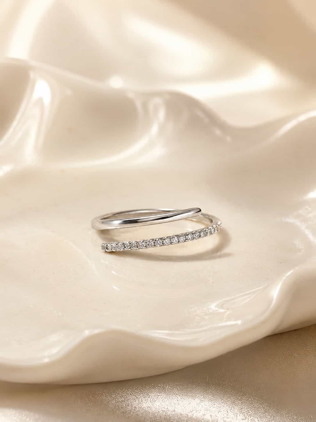 Close-up of the Naira double-row open wrap ring with a polished band and sparkling clear stones on a white ceramic tray
