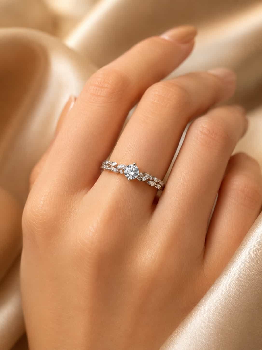 Woman wearing the Fiora floral solitaire-style ring with leaf-inspired side stones against champagne satin