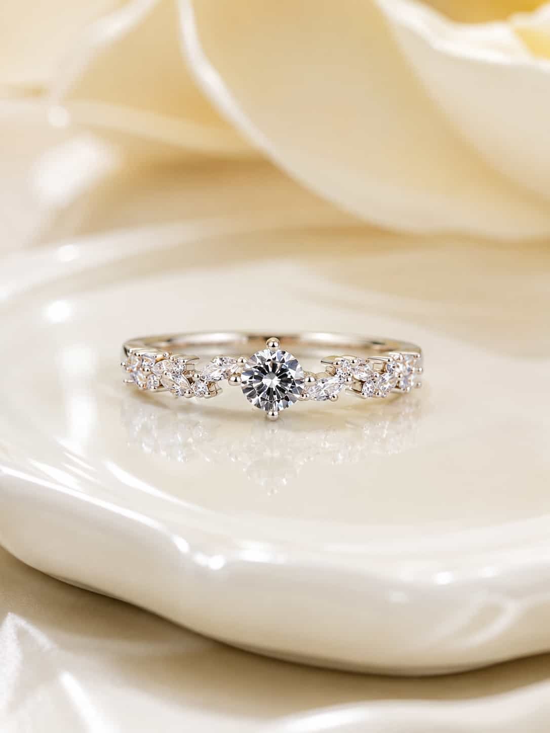 Close-up of Fiora platinum-polished floral ring with round centre stone and marquise vine detailing on a white ceramic tray