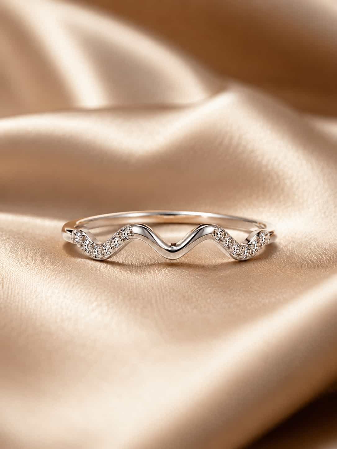 Serena wave sparkle ring displayed on champagne satin with its smooth platinum-polished centre curve in focus