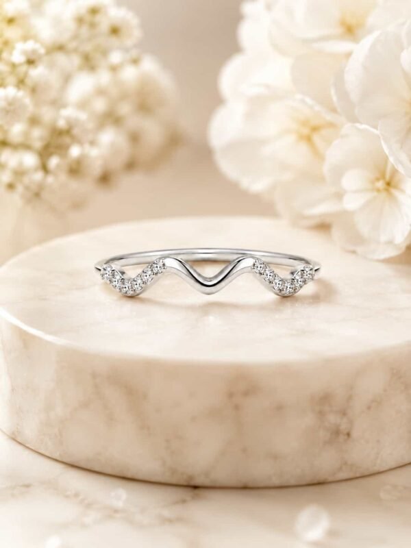 Serena platinum-polished wave ring displayed on a white marble pedestal with soft ivory flowers