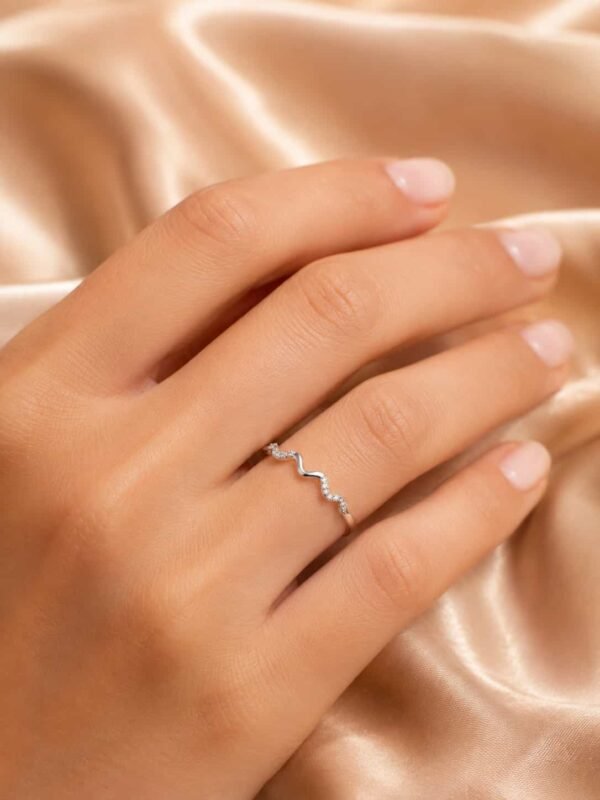 Woman wearing the Serena platinum-polished wave sparkle ring on her finger against champagne satin