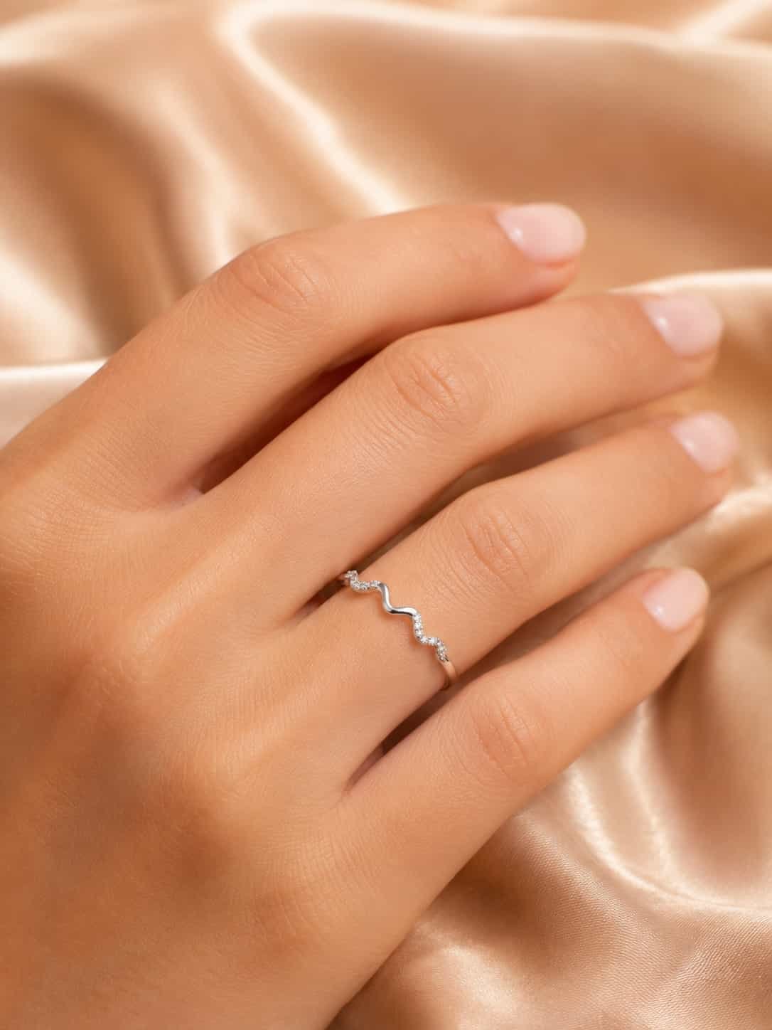 Woman wearing the Serena platinum-polished wave sparkle ring on her finger against champagne satin