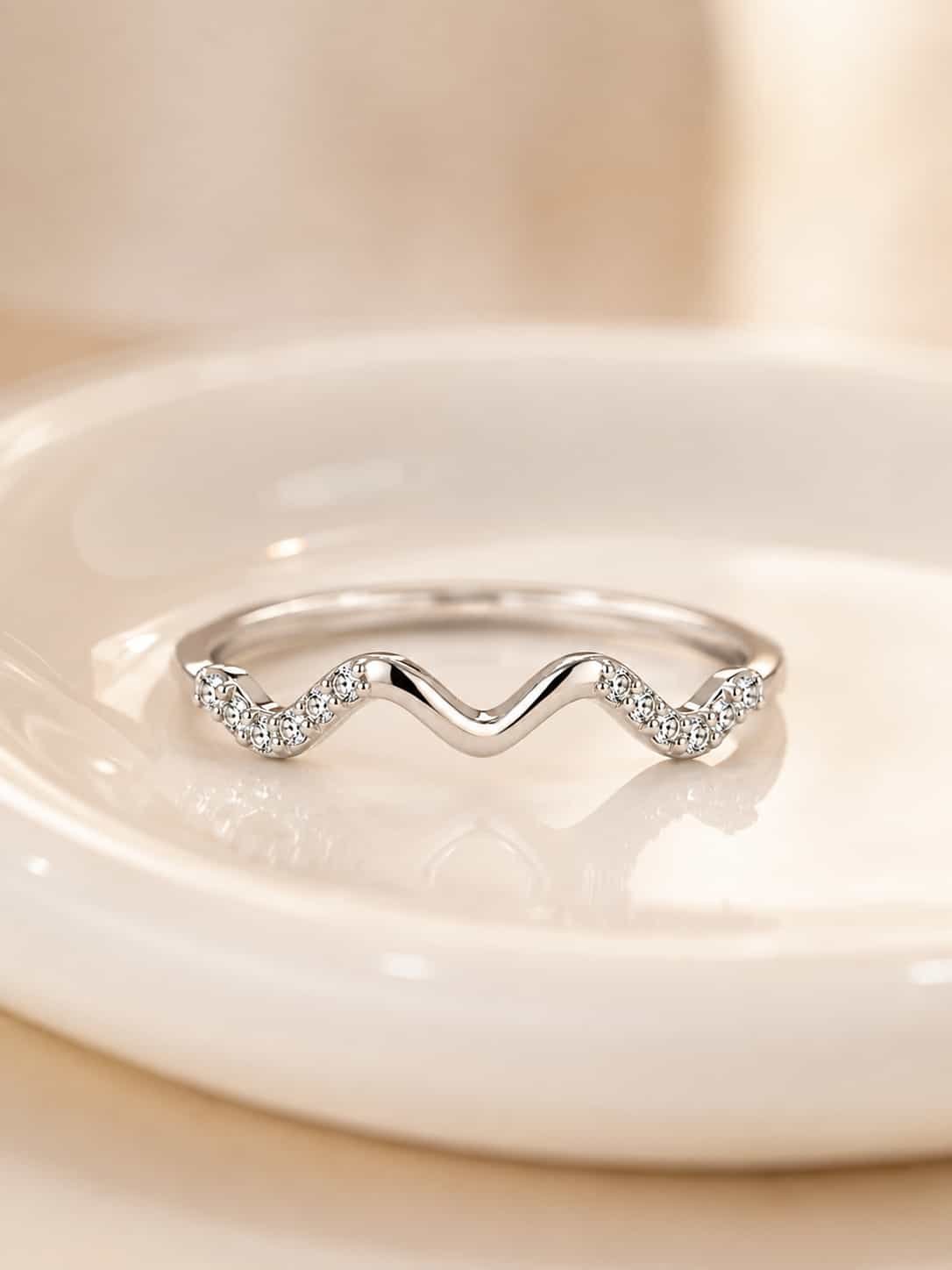 Close-up of Serena wave sparkle ring with a polished centre curve and clear stone detailing on a white ceramic tray