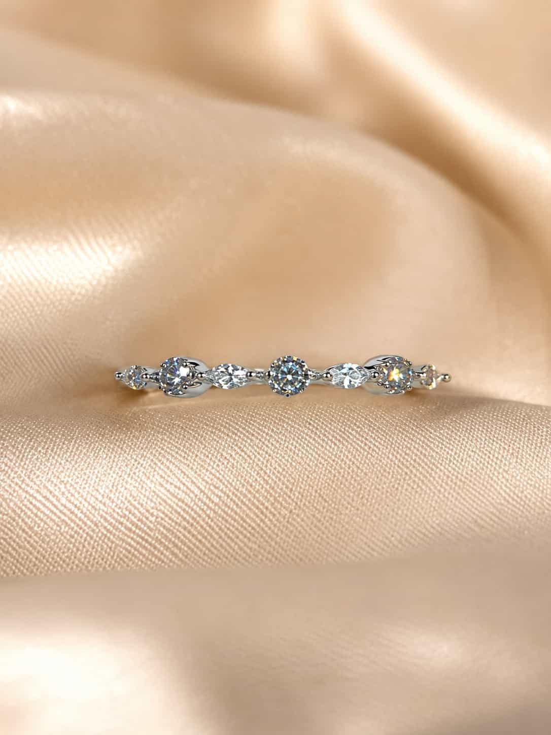 Liora round and marquise sparkle band ring displayed on champagne satin in warm light