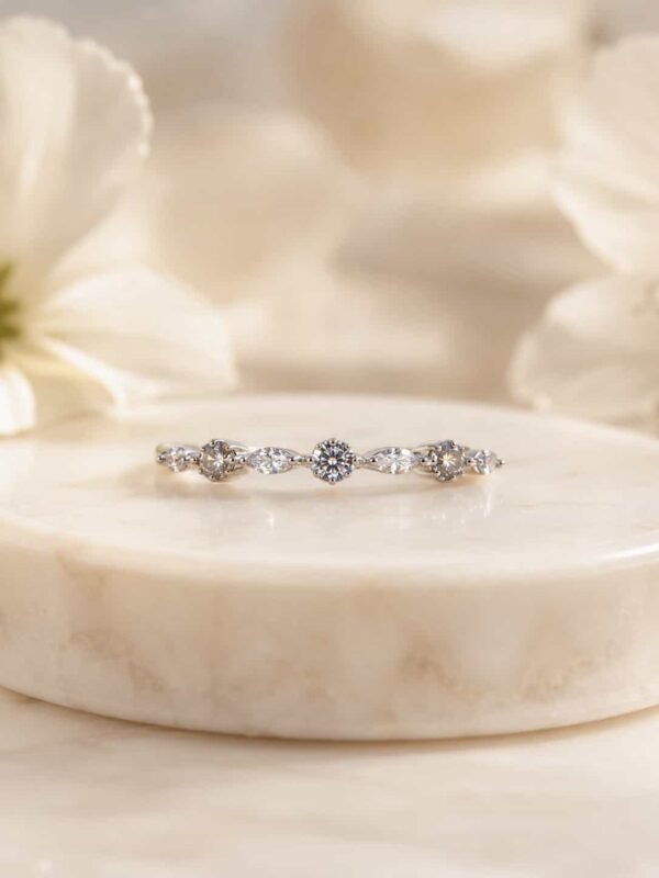 Liora platinum-polished round and marquise band ring on white marble with soft ivory flowers