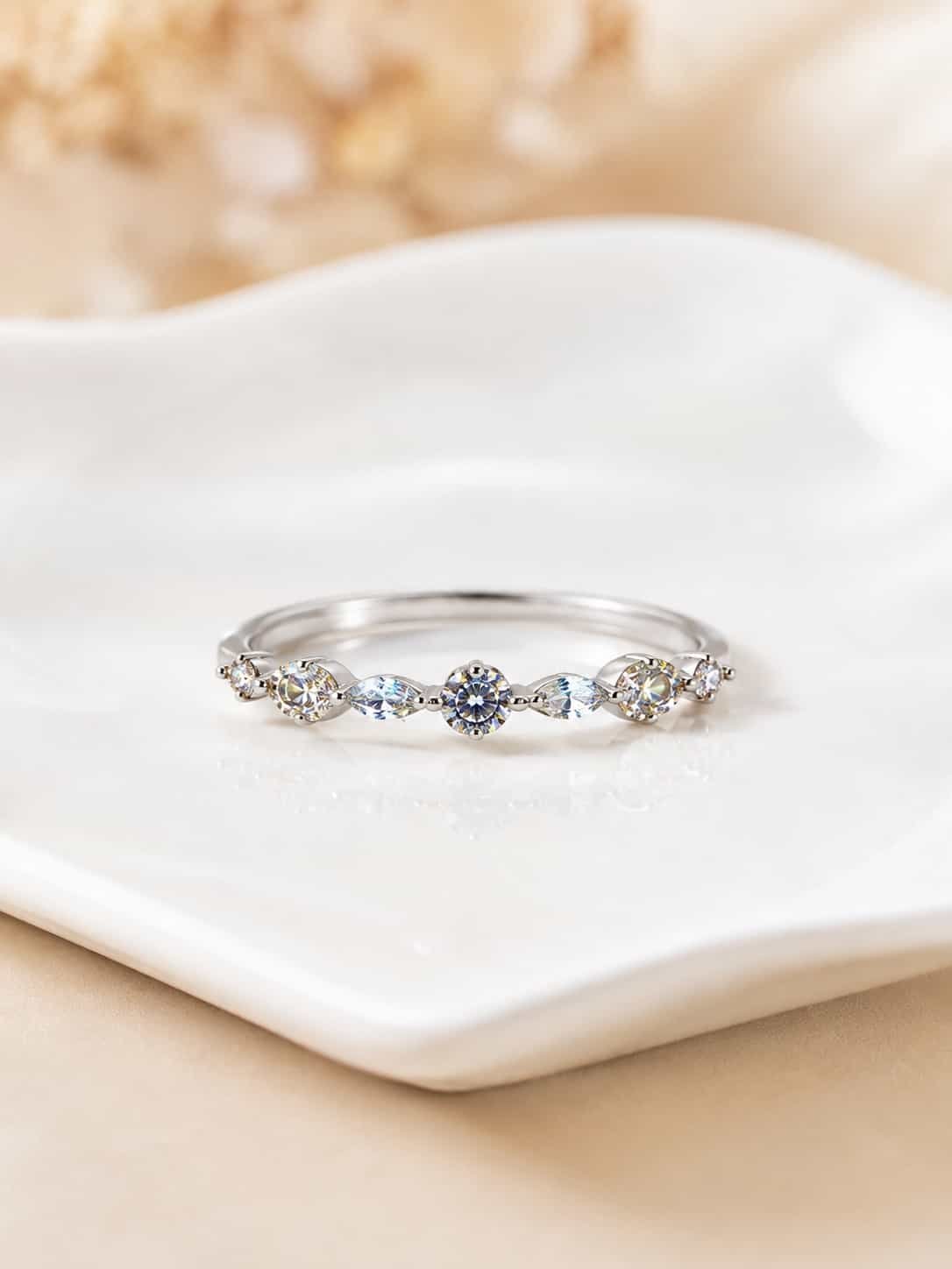 Close-up of Liora platinum-polished band ring with alternating round and marquise stones on a white ceramic tray