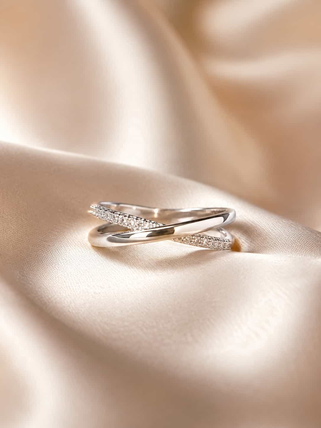 Elara criss-cross sparkle ring displayed on champagne satin with intertwined platinum-polished bands