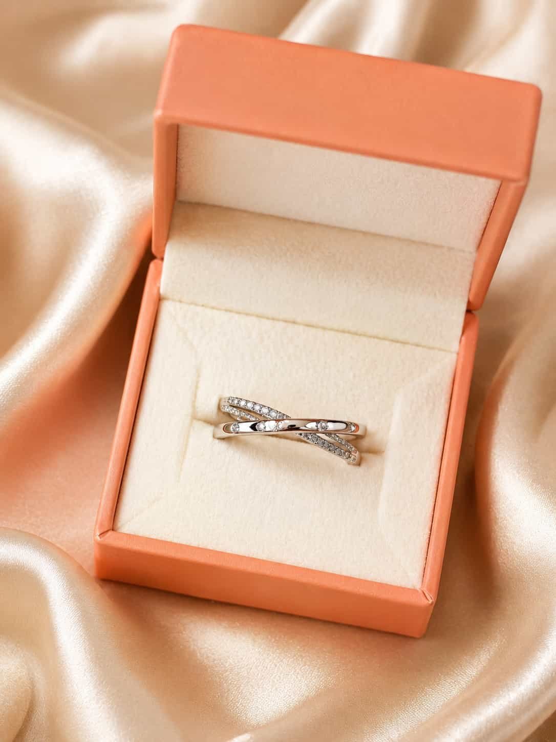Elara criss-cross sparkle ring presented inside an orange jewellery gift box on champagne satin