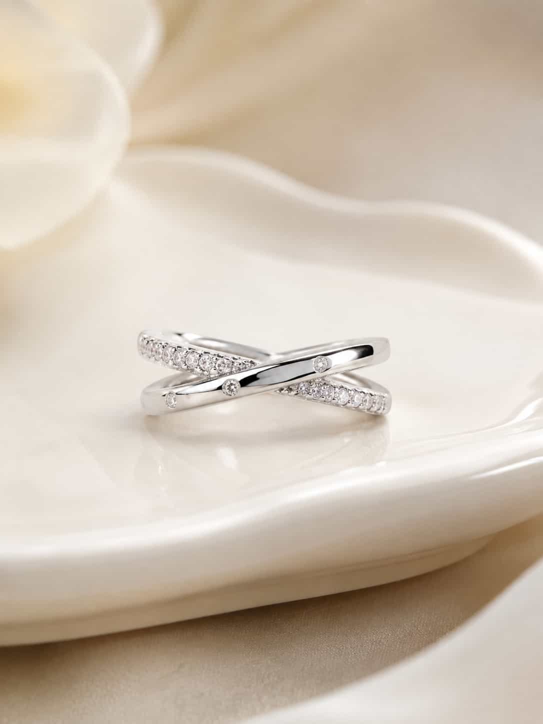 Close-up of Elara platinum-polished criss-cross ring with three clear accents and stone-studded bands on a white tray