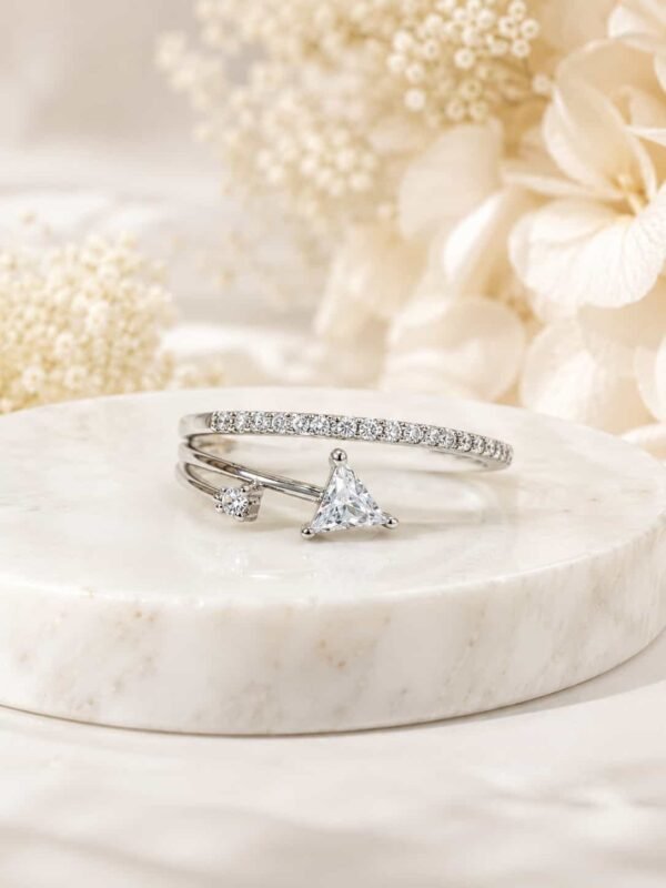 Evara platinum-polished triangle open ring displayed on a white marble pedestal with soft ivory flowers