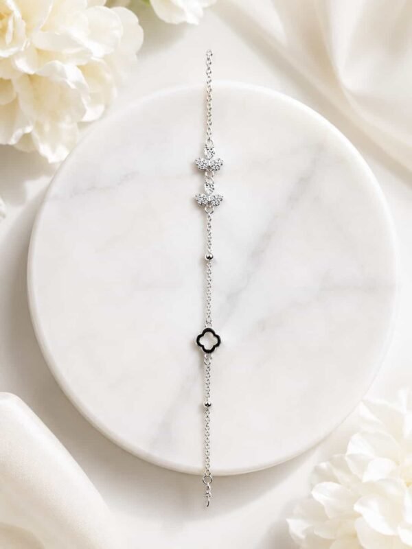 Full view of silver-tone butterfly and black clover bracelet displayed on white marble with floral styling