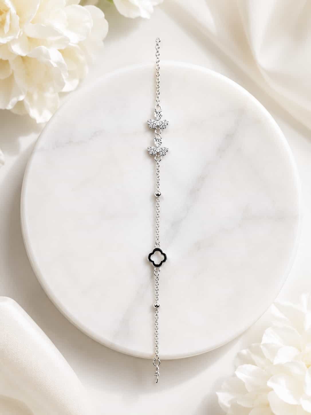 Full view of silver-tone butterfly and black clover bracelet displayed on white marble with floral styling