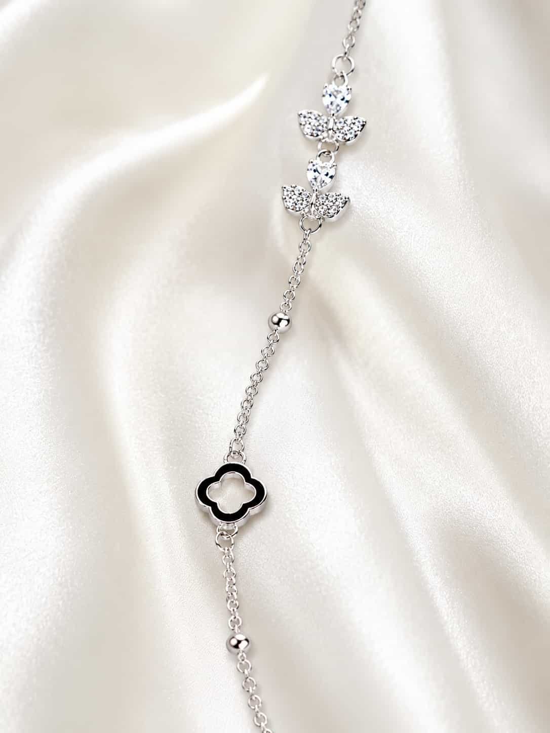Close-up of sparkling butterfly motifs and black clover detail on delicate silver-tone bracelet