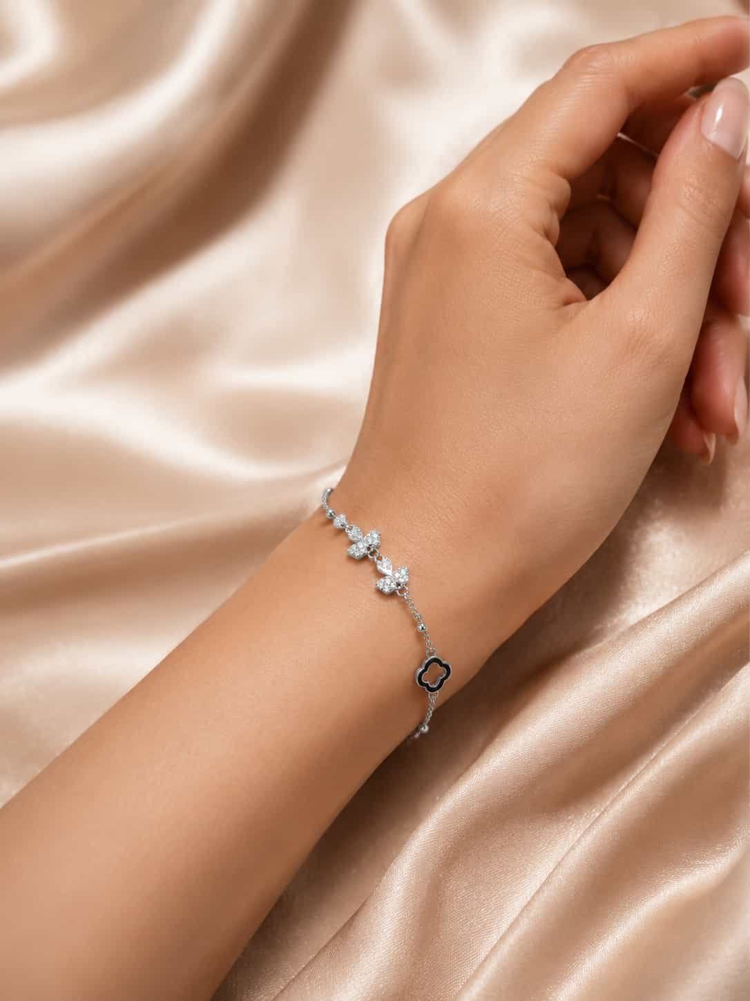 Woman wearing delicate silver-tone butterfly bracelet with sparkling stones and black clover charm