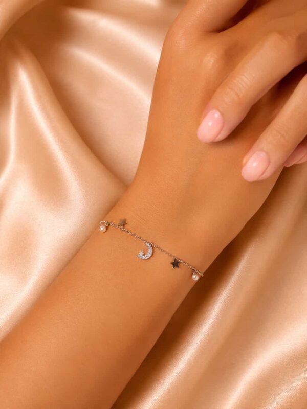 Woman wearing delicate moon, star and pearl charm bracelet with sparkling crescent centrepiece