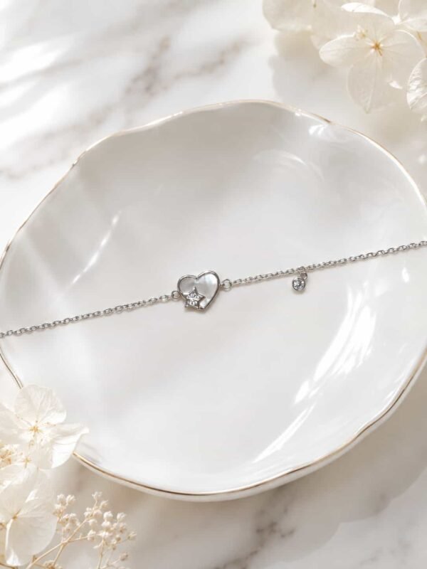 Delicate heart and star charm bracelet with pearlescent centrepiece displayed on a white ceramic jewellery dish