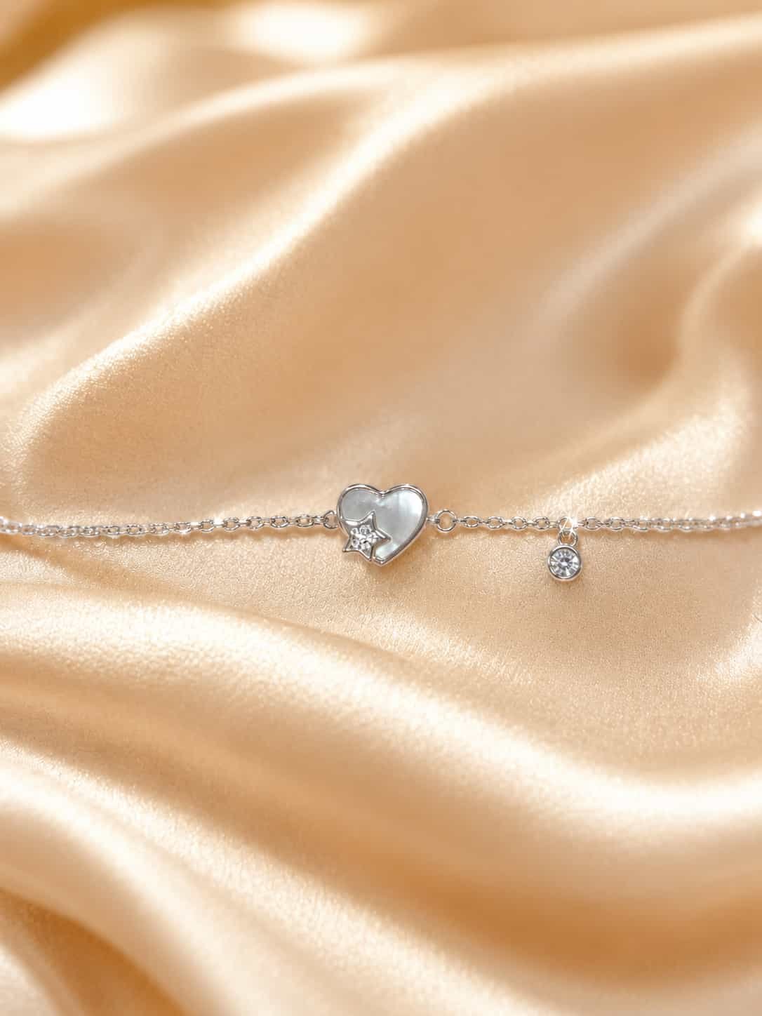 Close-up of Celestia pearlescent heart bracelet with sparkling star detail and round clear stone charm on satin