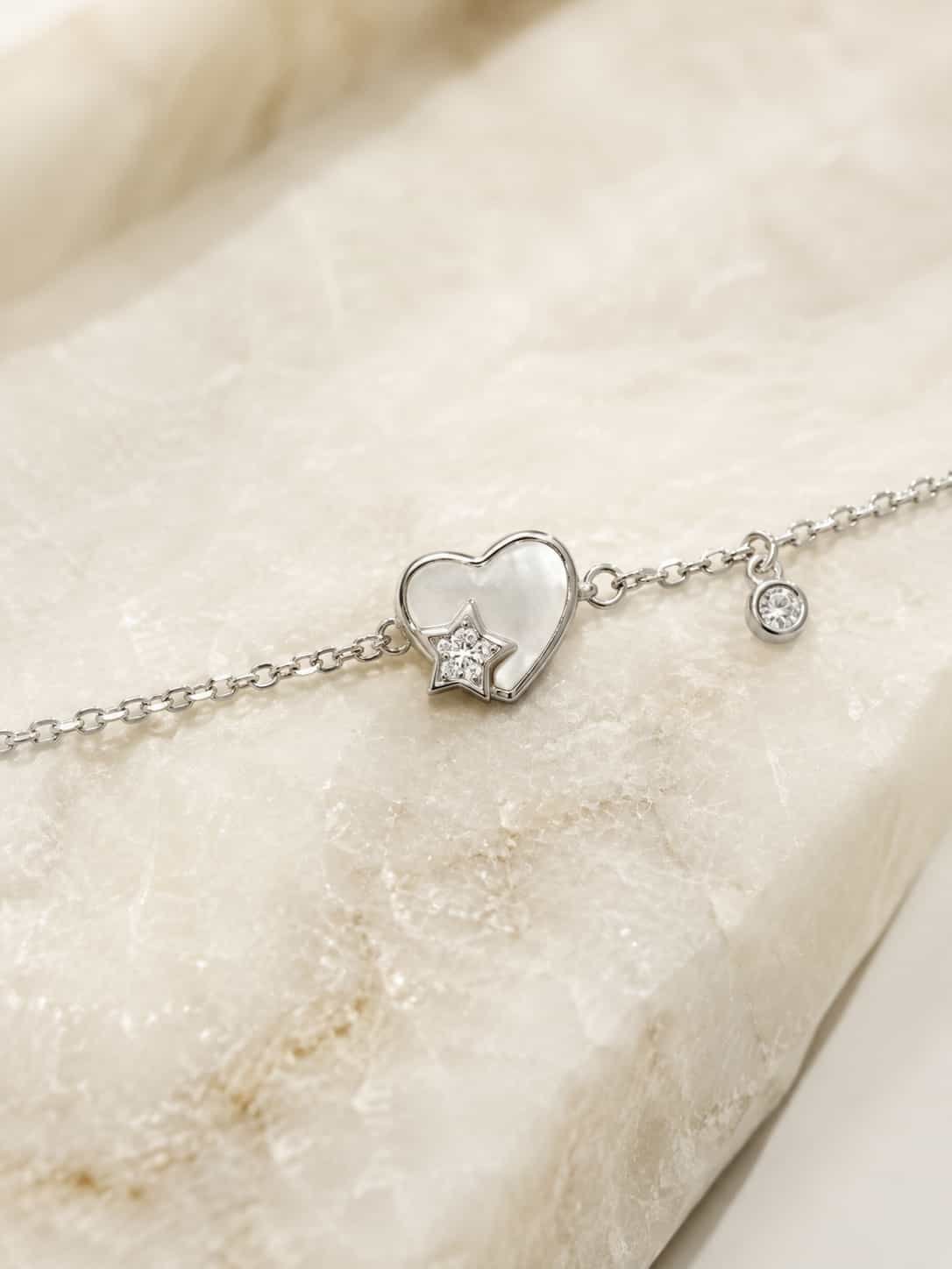 Macro view of pearlescent heart and sparkling star charm bracelet with delicate round stone pendant