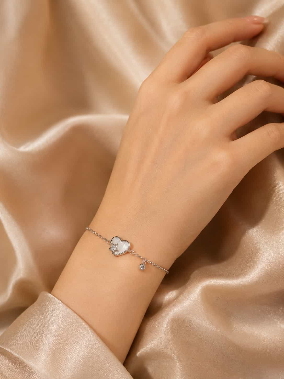 Celestia heart and star charm bracelet worn on a woman’s wrist with pearlescent heart and dangling stone charm