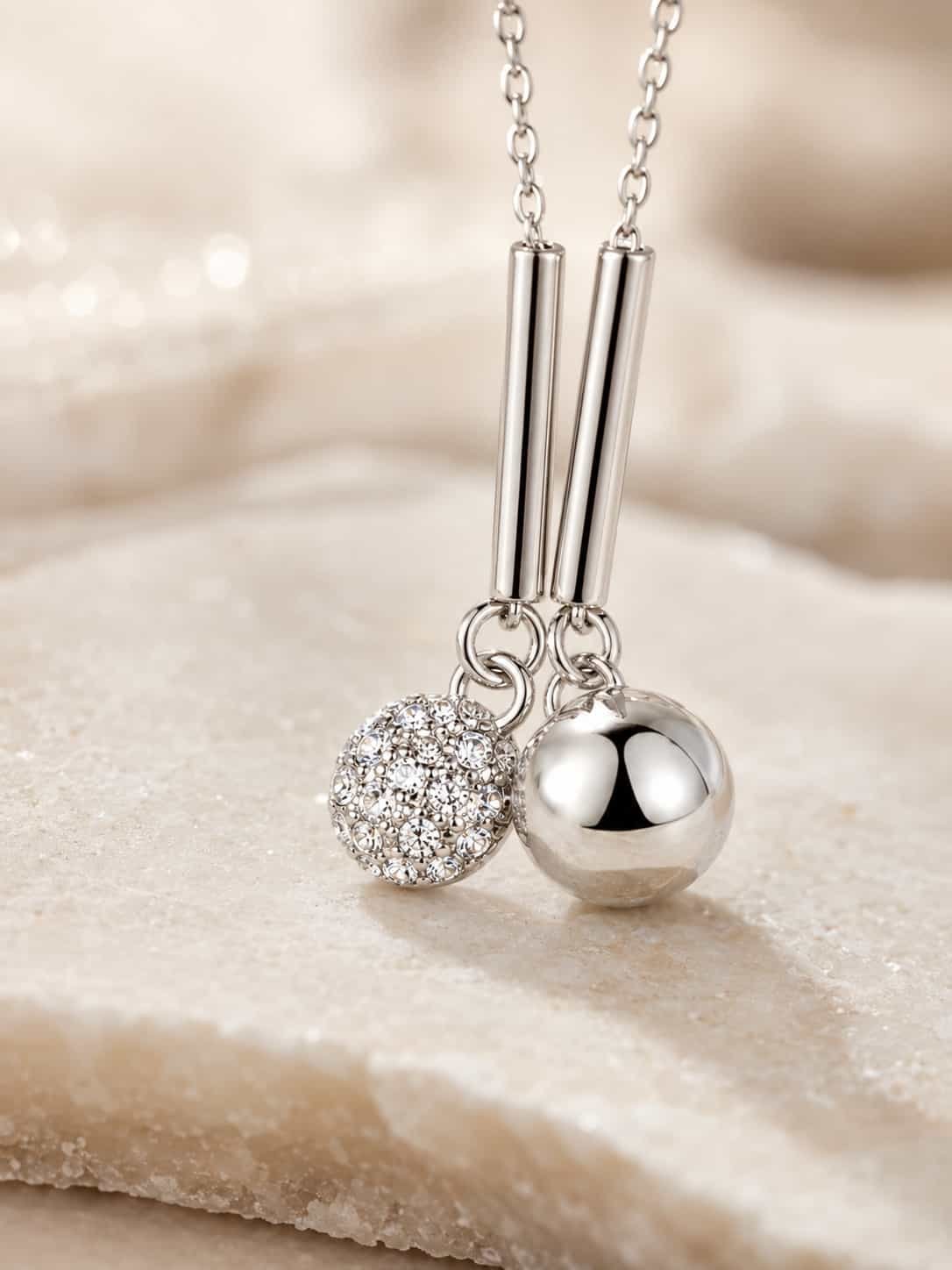 Close-up of twin sphere pendant with clear crystal-studded ball, mirror-polished ball and sleek silver-tone bar drops